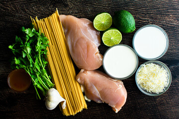 Wall Mural - Creamy Cilantro-Lime Chicken Pasta Ingredients: Spaghetti, chicken breast, and other raw ingredientson a wood table