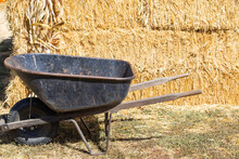 Wheelbarrow In Front Of A Stack Or Bale Of Hay On A Farm
