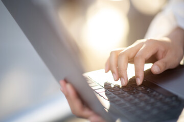 Wall Mural - Close-up of a woman's hand typing on a modern laptop keyboard. to take notes on the device Asian woman using computer equipment outdoors new technology concept.