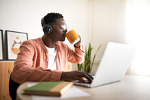 Young African American Black Man Drinking Coffee While Listening To Music And Working With Laptop. Working From Home.