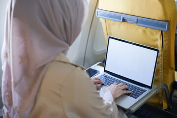 Wall Mural - Attractive muslim women passengers working on laptop sitting near window in an airplane.