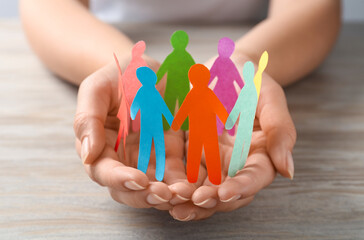 Woman holding paper human figures at wooden table, closeup. Diversity and inclusion concept
