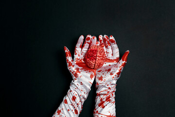Fototapeta creepy human brain in hands in bloody gloves on a black background.