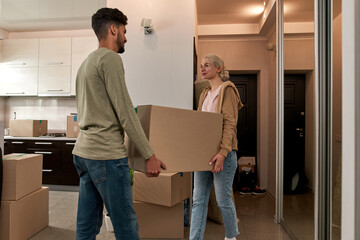 Young smiling couple carrying box in new apartment