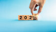© tete_escape - The calendar year 2022 changed to the new year 2022. Close-up hand turning number 2 to 3 on wooden the last cube block for the transition from 2022 to 2023 isolated on blue background, ready to begin.