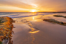 A Golden Sunset Over The Ocean Reflecting In A Wet Sandy Beach Between Rocks