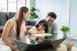 © SKW - Asian family portrait parents and daughter in the living room The daughter is doing homework with her father and mother giving advice and teaching closely.