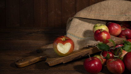 Wall Mural - Apple harvest background - Many colorful red ripe apples in jute sack and apple with carved heart symbol