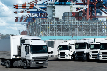 Aufkleber - Trucks in the international seaport against on a background of a ship loaded with containers. International trade and logistics concept