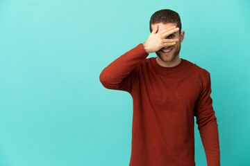 Wall Mural - Handsome blonde man over isolated blue background covering eyes by hands and smiling