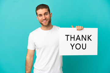 Handsome blonde man over isolated blue background holding a placard with text THANK YOU with happy expression