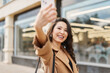 © olga pink - Glamour attractive asian kazakh female wearing beige coat, taking selfie, checking haircut, look at smartphone camera, walking on street