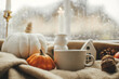 © sonyachny - Stylish warm cup of tea, candle, pumpkins on cozy wool blanket against window with rain drops. Moody fall wallpaper. Happy Thanksgiving. Autumn banner. Cozy autumn rainy day