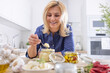 © weyo - Sniling blond woman picks a teaspoon of crushed garlic from a jar in the kitchen