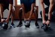 © StratfordProductions - Close-up of three muscular multiracial young adults doing kettlebell squats at the gym