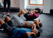 Group of multiracial young adults with trainer doing sit-ups at the gym