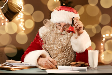 Wall Mural - Santa Claus with Christmas bell writing letter at table in evening