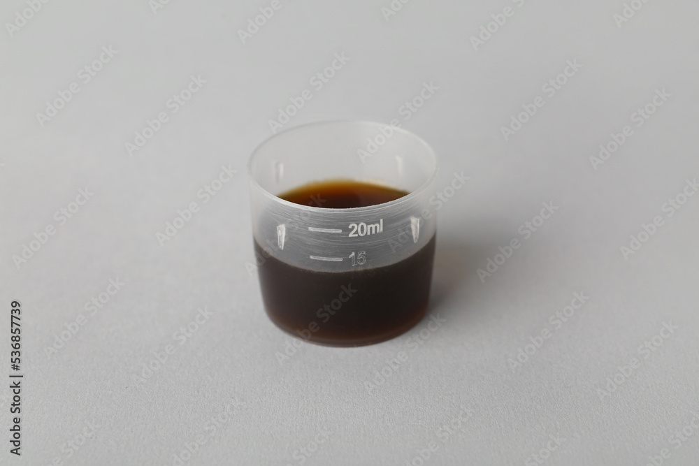 Measuring cup of cough syrup on grey background