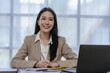 © ArLawKa - Asian businesswoman working on laptop computer with financial graph document in modern office near window with calculator and business report on desk
