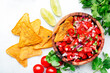 Mexican food. Spicy salsa sauce with tomatoes, chili peppers, onion, garlic and cilantro with nachos corn chips, white table background, top view