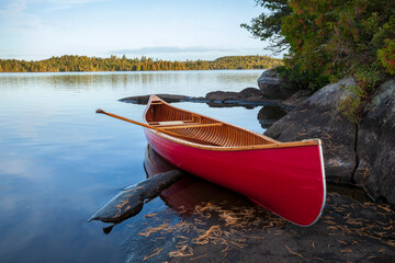 Wall Mural - red wood canoe on rocky shore of a boundary waters lake in morning light during autumn