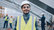 portrait of young Middle Eastern builder wearing uniform standing in construction site smiling and looking at camera. People and occupation concept.