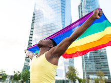 Young Man Wearing Yellow Vest Holding Rainbow Flag In Front Of Skyscrapers