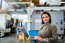 Smiling Mature Businesswoman Holding Laptop In Industry