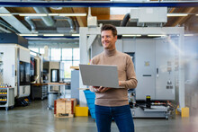 Smiling Businessman Holding Laptop In Industry