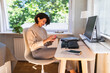 © Westend61 - Smiling businesswoman using smart phone in front of desktop PC on table at home