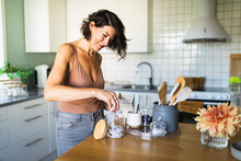 Happy Woman Filling Glass Jar At Kitchen Counter