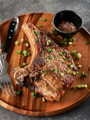 Wall Mural - Grilled pork chop on grey plate sprinkled with green onions on the wooden plate, grey background