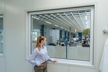 Young Businesswoman With Hand In Pocket Looking Through Window At Warehouse