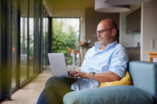 Man Using Laptop Sitting On Sofa At Home