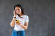 © Westend61 - Smiling woman holding smart phone and listening to music through wireless headphones in front of gray wall