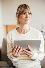 Thoughtful Pregnant Woman Holding Tablet PC At Home