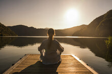 Woman Meditating On Jetty Over Lake At Vacation