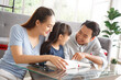 © aekkorn - Children education and home school concept : Young asian father and mother see little daughters' study. Excited smiling small child girl enjoying learning and reading with pleasant dad and mom at home
