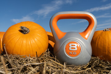 Heavy kettlebell and orange pumpkins on the hay. Healthy fitness lifestyle autumn fall composition for Halloween or Thanksgiving. Gym workout and sport training concept on a pumpkin patch farm.