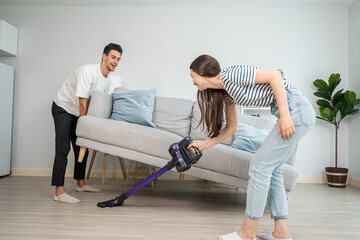 Sticker - Caucasian young man and woman cleaning living room together at home.