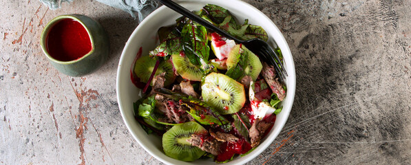 Wall Mural - bowl with salad with duck breast and kiwi with raspberry sauce on the table