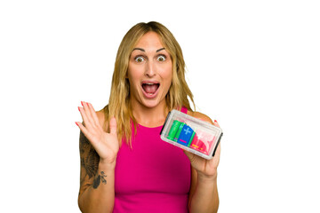 Young caucasian woman holding battery box isolated on green chroma background surprised and shocked.