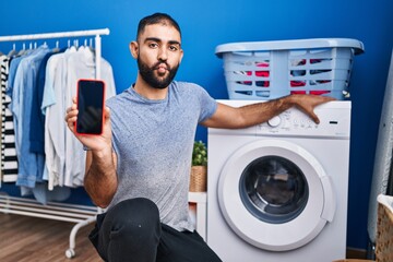 Sticker - Middle east man with beard showing smartphone screen and washing machine making fish face with mouth and squinting eyes, crazy and comical.