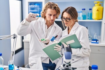 Wall Mural - Man and woman wearing scientist uniform holding pills writing on notebook at laboratory