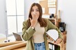 © Krakenimages.com - Young brunette woman holding architect hardhat at the office covering mouth with hand, shocked and afraid for mistake. surprised expression