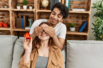 Sticker - Young couple smiling happy sitting on the sofa holding engagement ring  at home.