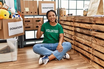 Wall Mural - Young african american woman wearing volunteer t shirt at donations stand showing and pointing up with finger number one while smiling confident and happy.