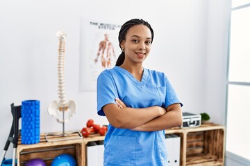 Canvas Print - Young african american woman wearing physio therapist uniform standing with arms crossed gesture at clinic