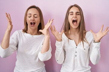 Wall Mural - Middle age mother and young daughter standing over pink background celebrating mad and crazy for success with arms raised and closed eyes screaming excited. winner concept