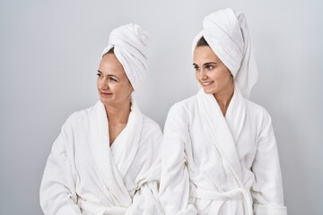 Canvas Print - Middle age woman and daughter wearing white bathrobe and towel looking away to side with smile on face, natural expression. laughing confident.